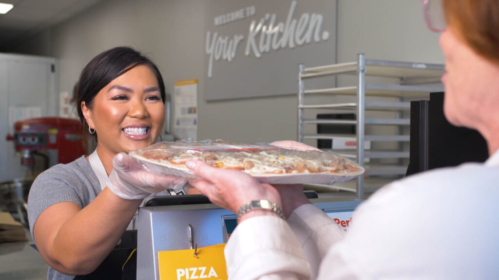 smiling staff handing pizza first franchise