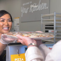 smiling while handing pizza to customer